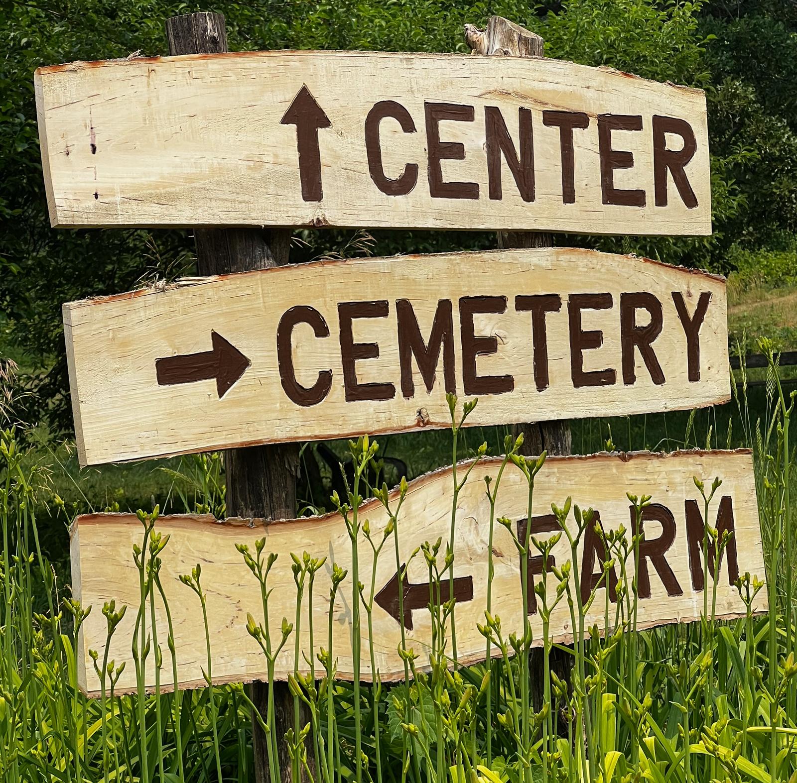 A wooden sign with panels that read 'Center', 'Cemetery', and 'Farm.'